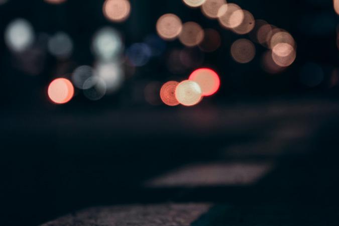 Blurry night photo of scattered lights and a closeup of dashed white lines on pavement