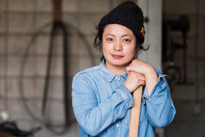 Woman in a blue shirt and black touque leaning on a long piece of wood